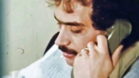 Vintage closeup of mustached man with curly hair talking on retro rotary phone