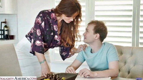 Brunette MILF in floral top leans seductively over seated guy touching his shoulder