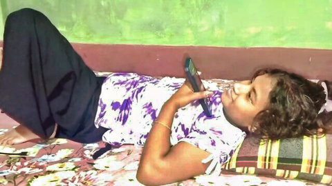 Sexy Indian girl with long curly hair lying on bed in tight top and pants holding phone seductively
