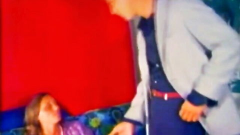 Vintage couple scene: suited man leans over woman in purple dress on couch, teasing hairy pussy vibe
