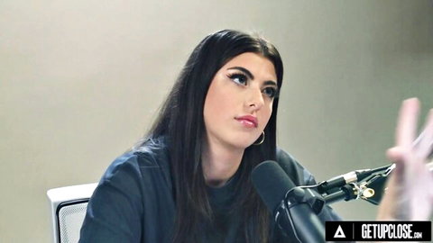 Young brunette with long dark hair gesturing hands near microphone in podcast interview