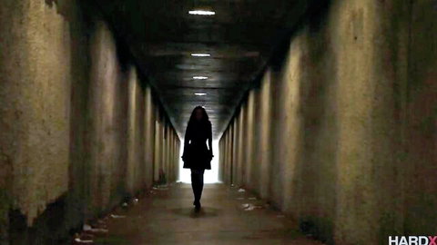 Brunette with long hair and curvy ass walks seductively down dark tunnel in heels
