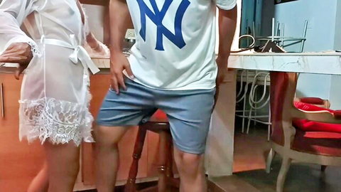 Sexy woman in sheer lace robe teases next to stud in NY Yankees shirt in kitchen.