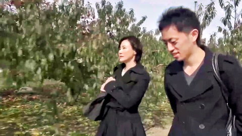 Asian stepmom in black coat walks with stepson in park, steamy preview