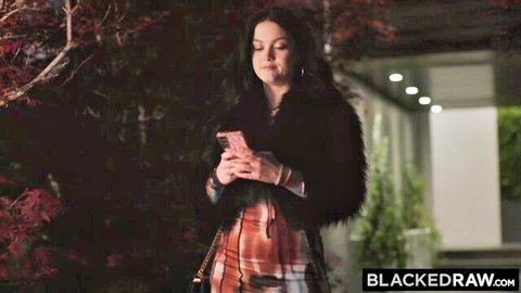 Brunette in black fur jacket and plaid skirt holds phone outdoors at night for BlackedRaw