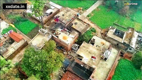 Aerial drone view of rural Indian village rooftops with laundry, green fields, trees and houses
