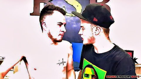 Shirtless tattooed young guy stares intensely at capped twink in bisexual tease