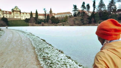 Person in orange beanie and yellow jacket views frozen lake and snowy castle landscape
