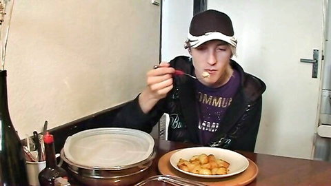 Young guy in purple hoodie and cap eats fried potatoes from plate at kitchen table