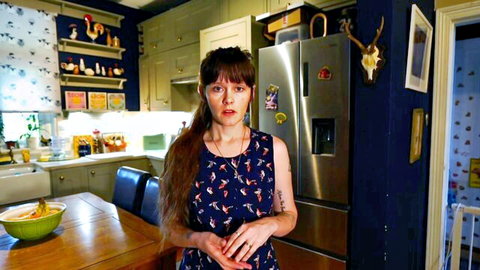 Curvy brunette MILF in floral dress standing in cozy kitchen with hands clasped teasing viewers