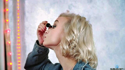 Petite blonde applying mascara in mirror with pink LED lights, sexy pout lips