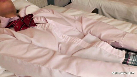 Asian schoolgirl in pink uniform and bowtie lying seductively on bed