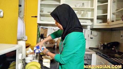 Clothed hijabi Indian woman pouring milk into glass in kitchen teasing curves