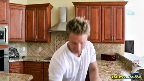 Blonde guy in white t-shirt stands in modern kitchen with Reality Kings watermark