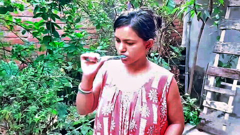 Sexy Indian woman brushing teeth with green toothbrush and foamy mouth in lush outdoor garden