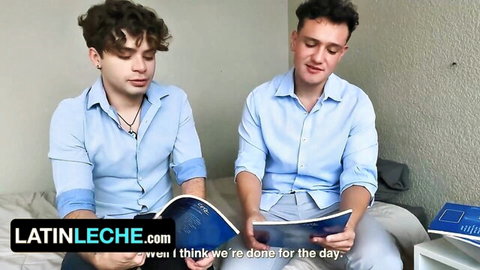 Two young Latino guys in blue shirts on bed holding books, casual gay scene