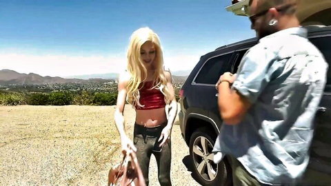 Sexy long-haired blonde in red crop top and tight jeans flirts with shirtless guy by black SUV outdoors