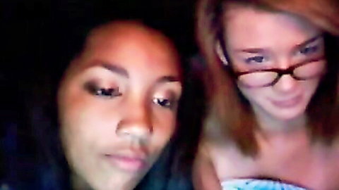 Closeup of sexy ebony woman and redhead teen with glasses posing intimately on webcam