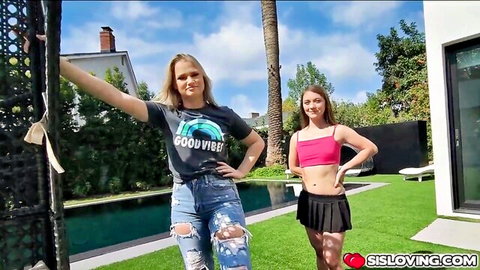 Blonde stepsister in Good Vibes tee and ripped jeans poses with brunette teen in pink crop top mini skirt poolside