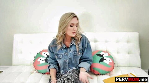 Blonde MILF in open denim jacket teases seductively on couch with flamingo pillows