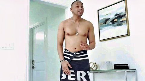Muscular shirtless black man standing in sarong gesturing indoors