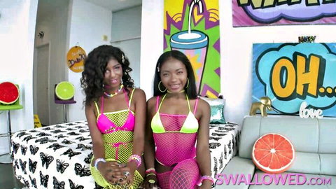 Two sexy young ebony babes in sheer pink and white fishnet bodysuits posing seductively on bed
