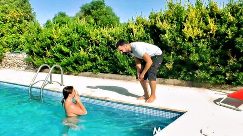 Amateur babe naked in pool covers eyes playfully as guy in shorts bends over pool edge teasing her