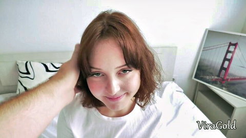 Red-haired Liza Ginger smiling with hand on head in white t-shirt