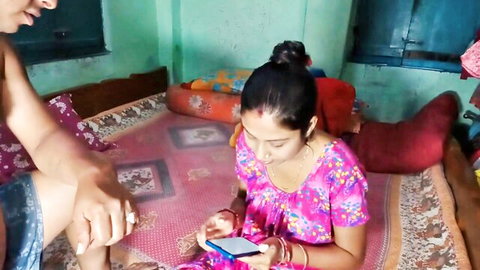 Indian stepmom vabi in pink floral dress sits on bed holding phone intimately