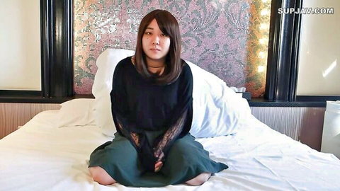 Seductive Asian woman in black lace top and green skirt sitting on bed with pillows