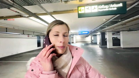 Blonde woman in pink jacket talking on phone in empty parking garage