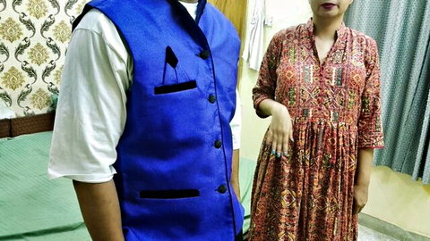 Indian man in blue vest and woman in red printed dress standing side by side in bedroom