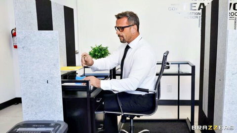 Mature suited businessman in glasses sits at office desk holding small plant in cubicle