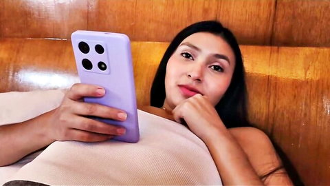 Curvy Latina stepsister holding phone in bed, teasing with cleavage