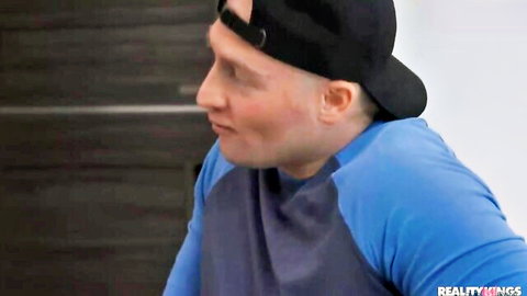Bald man in backwards black cap smirks sideways wearing blue raglan shirt in Reality Kings porn scene