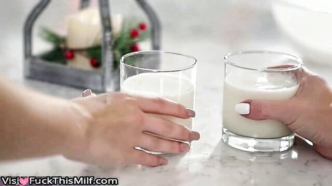 Two feminine hands with white nails holding glasses of creamy white milk on festive table