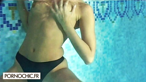 Blonde woman underwater, topless and covering breasts in pool
