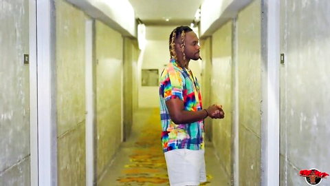 Black man with dreads in colorful shirt and white shorts standing in hotel hallway