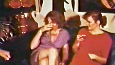 Retro 70s pornstars in sexy purple and red dresses sharing drinks intimately