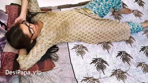 Desi Bhabhi in beige kurta and blue pants lying on bed, glasses on