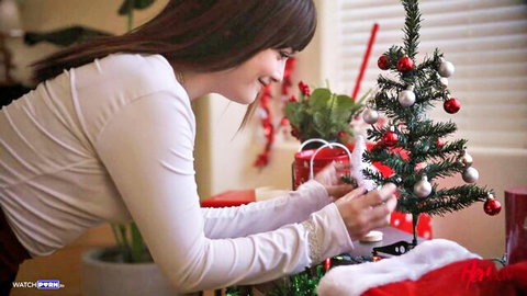 Brunette babe in white blouse leans over decorating tiny Xmas tree smiling naughtily