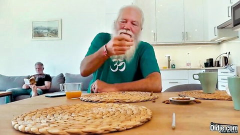 Bearded old man in green Om shirt sits at kitchen table with coffee cups