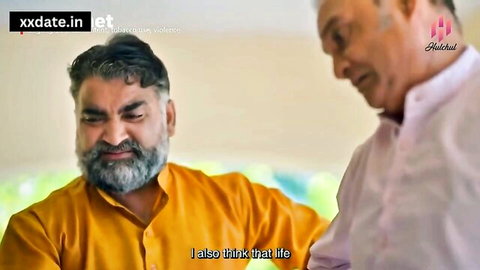 Two mature bearded Indian men in saffron and pink shirts talking seriously.