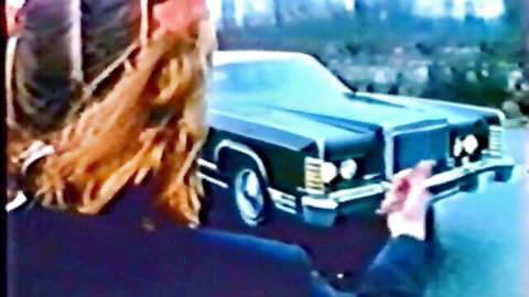Vintage German blonde in boots and pigtails teases lover by black car outdoors