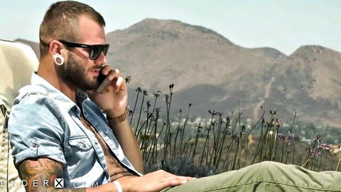 Johnny Hill lounging outdoors in open denim shirt, tattoos and beard on display
