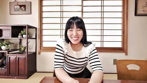 Smiling Japanese girl in frilly striped blouse and black skirt leaning forward at table