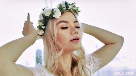 Blonde MILF in flower crown and sheer lace top raises arms seductively teasing curves