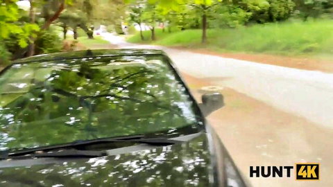 Black car on dirt road surrounded by green trees in outdoor public setting