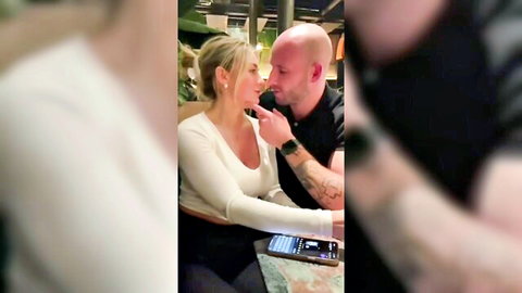 Blonde woman with long hair passionately kissing bald tattooed man in steamy lounge embrace