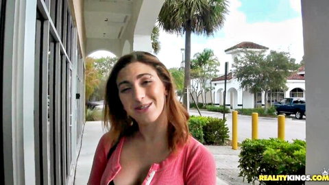 Brunette smiling with deep cleavage spilling from open pink cardigan outdoors